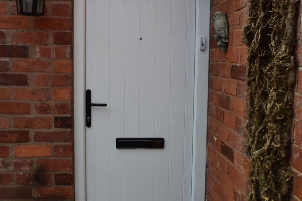 White uPVC residential door with a black handle on a red brick building