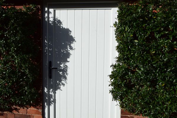 White wood style uPVC residential door between two green bushes on a red brick building